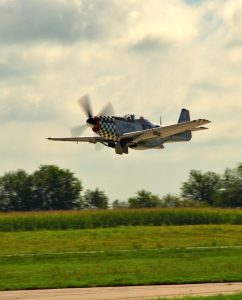 World War II era single-propeller fighter plane landing. The nose and tips of wings have checkerboard pattern..