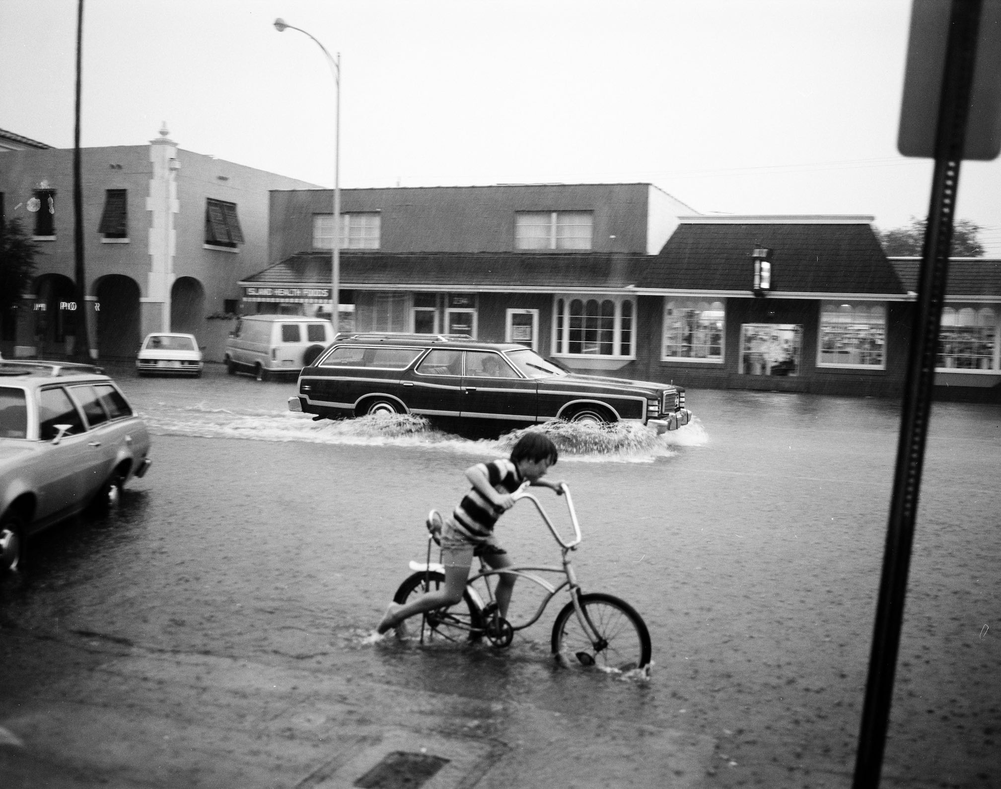 Boy riding bicycle through storm water through commercial street.