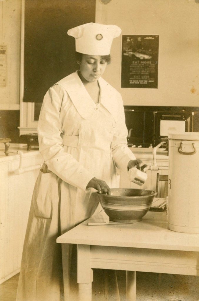 Blanche Armwood in an apron and chef’s toque pours flour into a bowl. Unknown, "Blanche Armwood Baking" (1915). Armwood Family - Photographs. Image 4.