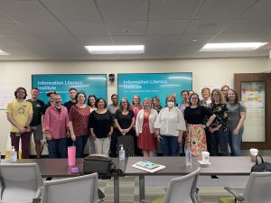 A group of 20 people smiling for the camera. the group is indoors in what appears to be a classroom-type setting.