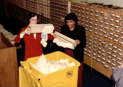 Library staff emptying card catalog drawers into recycling bin.