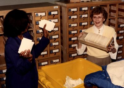 Library staff emptying card catalog drawers into recycling bin.