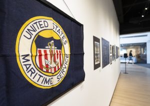 blue flag with round seal reading United States Maritime Service hangs on a wall